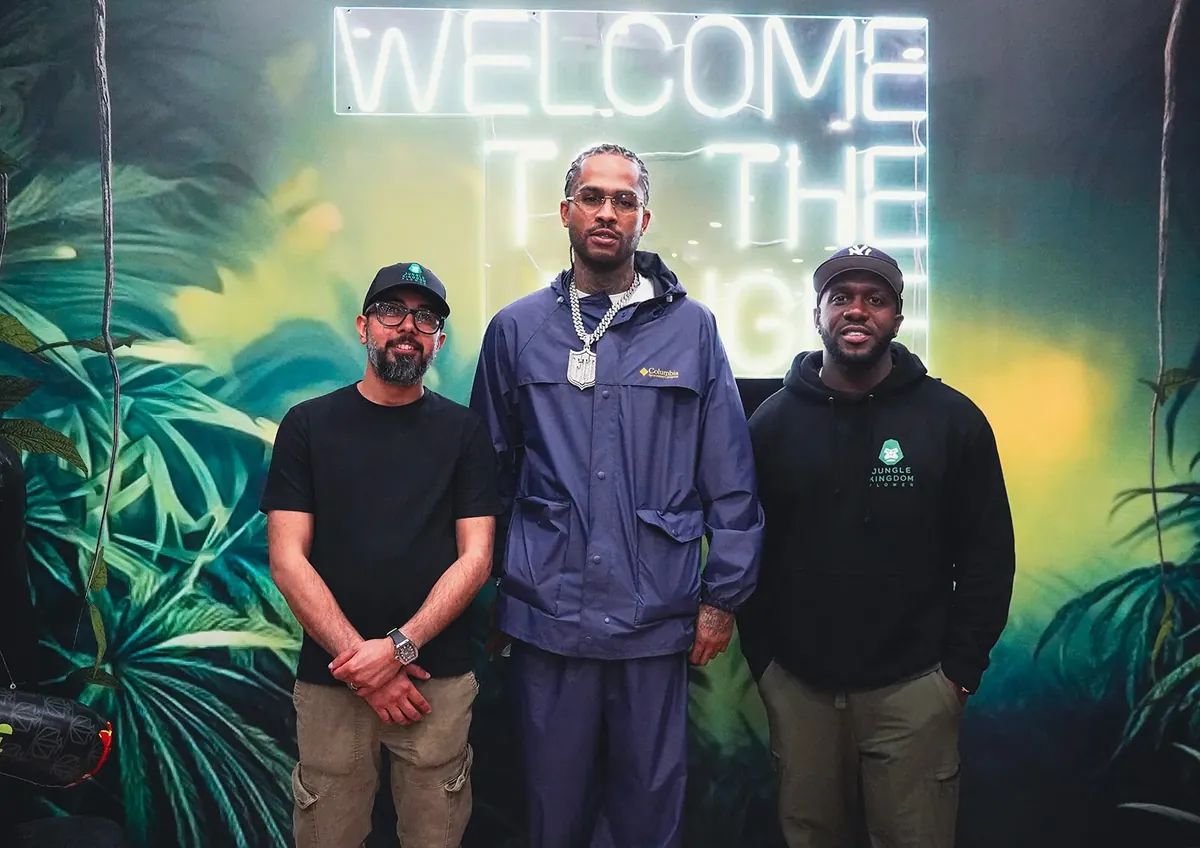 Three people pose under the neon Welcome to the Jungle sign, in front of a hand-painted jungle mural inside Jungle Kingdom Flower